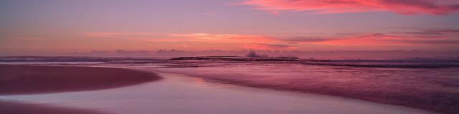 A beach at sunset with pink and purple clouds.