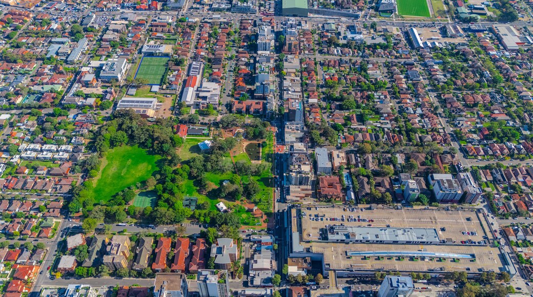 An aerial view of a densely populated urban area with residential buildings, a large green park, and a sports field.