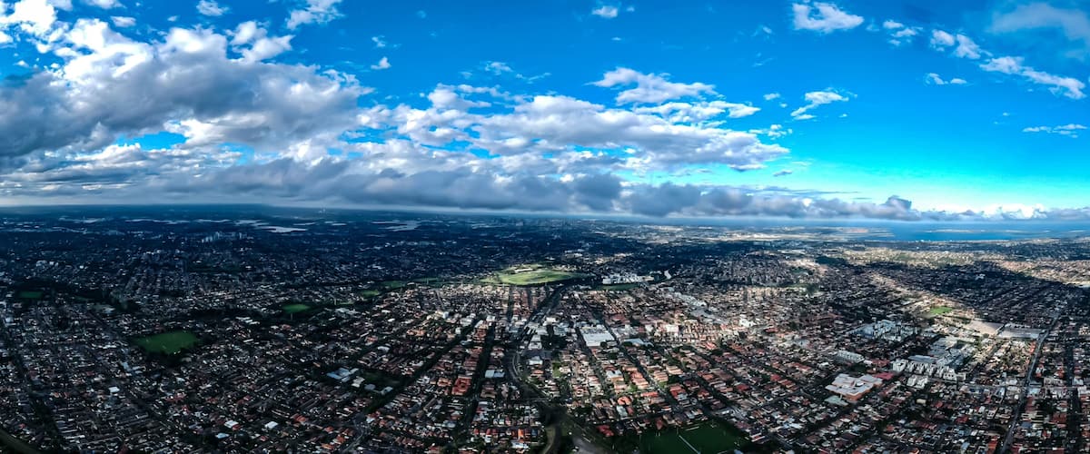 Eine weite Panoramatansicht einer dicht bebauten Stadt, eines Flusses und eines weiter Wasserflächen im Hintergrund.