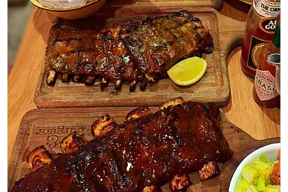A wooden table with barbecued ribs, fries, and a salad.