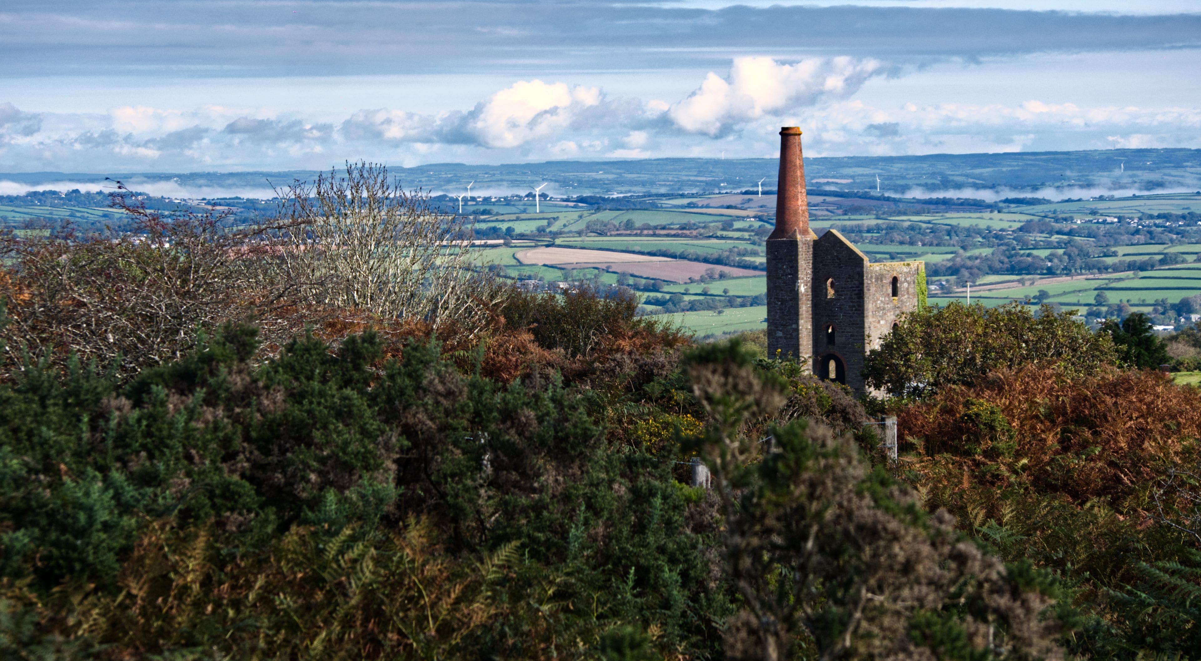 A rural landscape with a stone tower, wind turbines, and rolling fields.