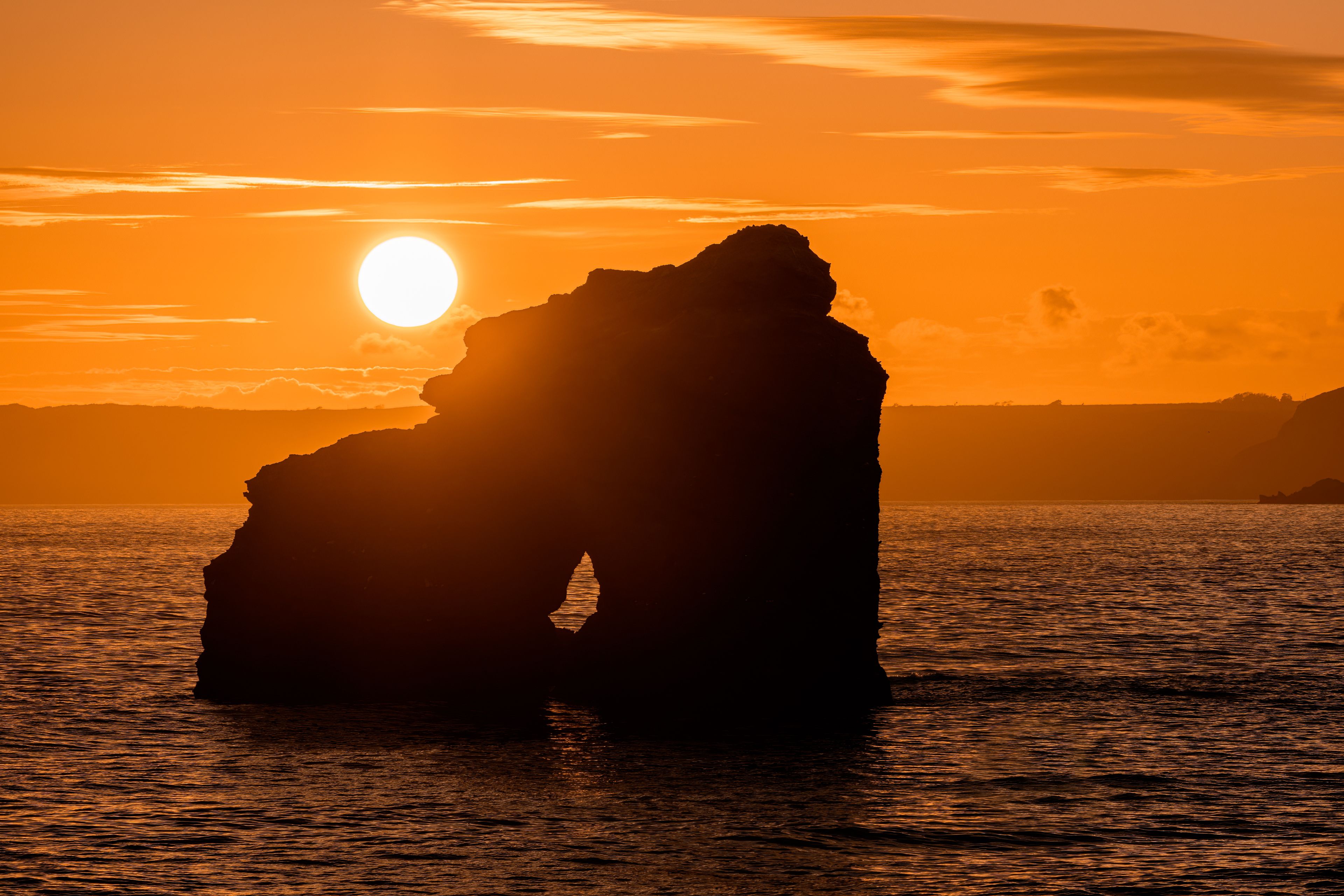 Une formation rocheuse se détachant sur le ciel au coucher du soleil, avec le soleil visible.
