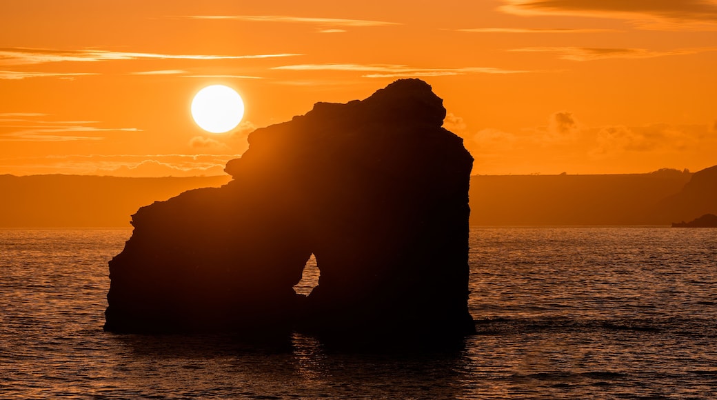 Une formation rocheuse se détachant sur le ciel au coucher du soleil, avec le soleil visible.