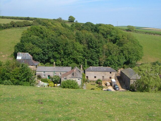 A rural landscape with a cluster of houses surrounded by lush greenery and rolling hills.
