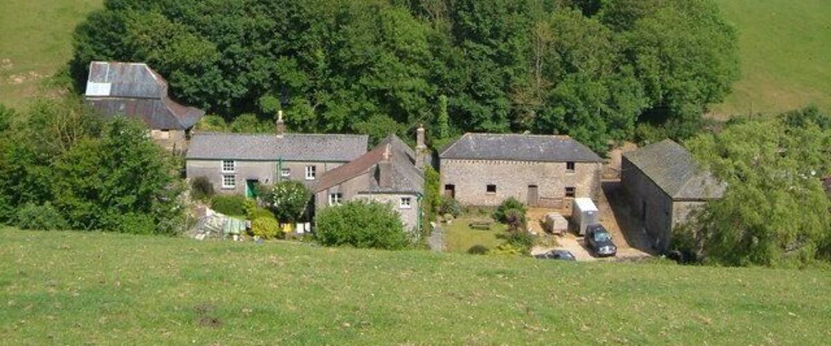 A rural landscape with a cluster of houses surrounded by lush greenery and rolling hills.