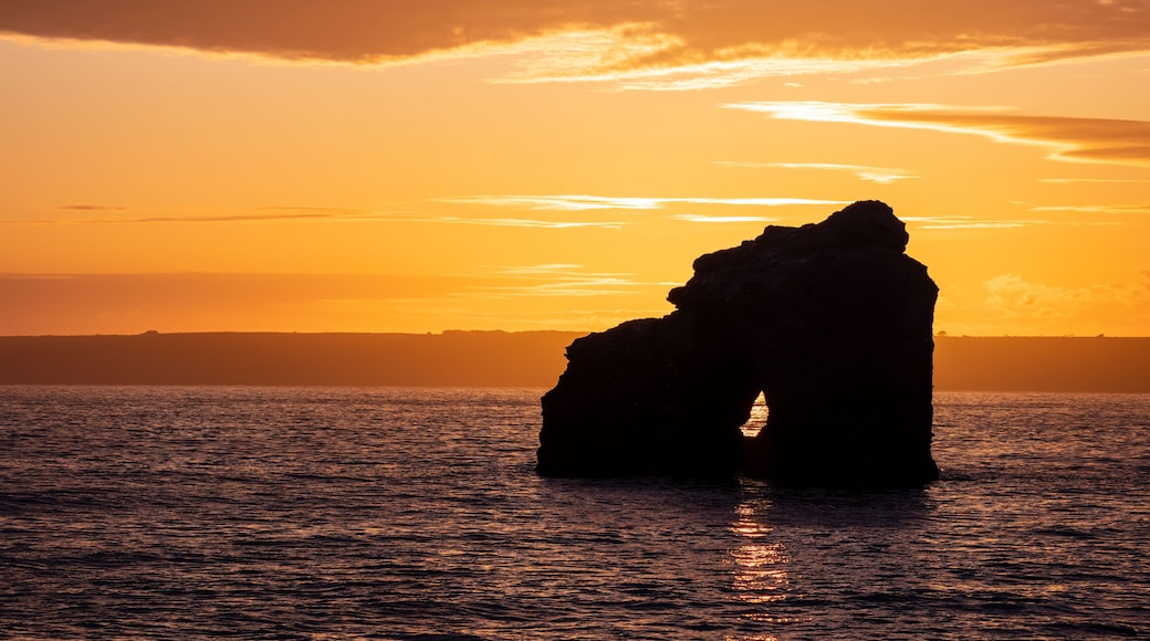 Une formation rocheuse se détachant sur le ciel d’un coucher de soleil, avec une mer calme au premier plan.