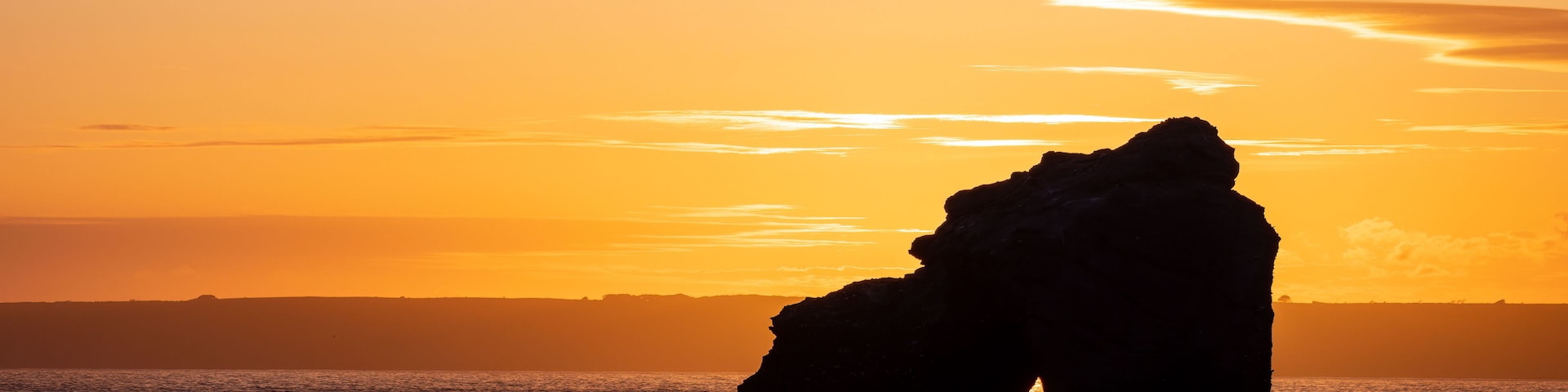Une formation rocheuse se détachant sur le ciel d’un coucher de soleil, avec une mer calme au premier plan.