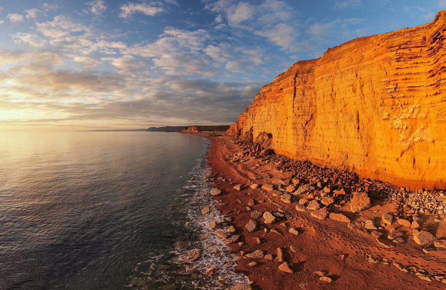 A coastal landscape with a prominent cliff, a sandy beach, and the ocean.