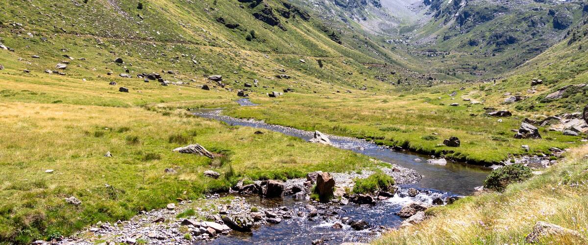 A mountain valley with a stream, rocky terrain, and grassy slopes.