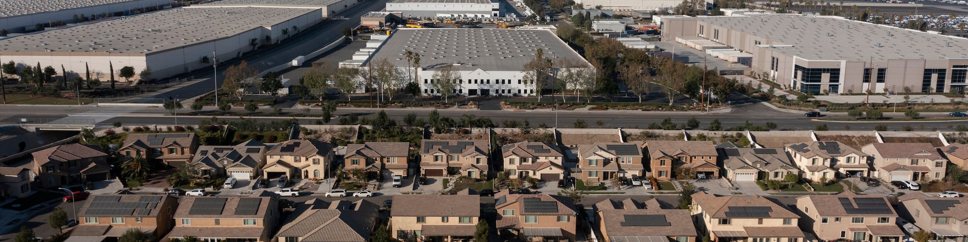 Jurupa Valley, California, USA - November 9, 2024: Afternoon sun shines on newly constructed industrial warehouses and suburban homes.