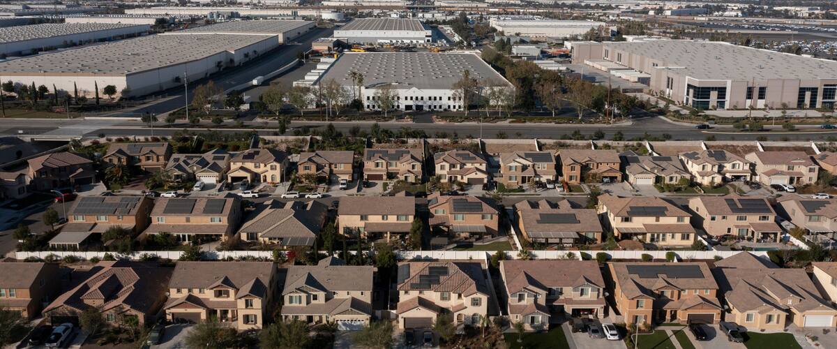 A residential area with houses, a large industrial building, and mountains in the background.
