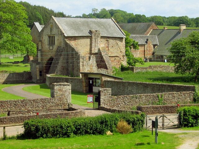 A stone building with a thatched roof, surrounded by a stone wall and lush greenery.