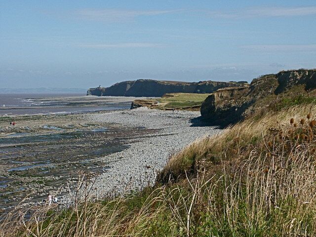 A pebbly beach with grassy dunes and cliffs in the background.