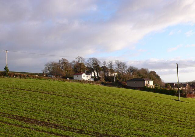 A rural landscape with a green field, white houses, and a cloudy sky.