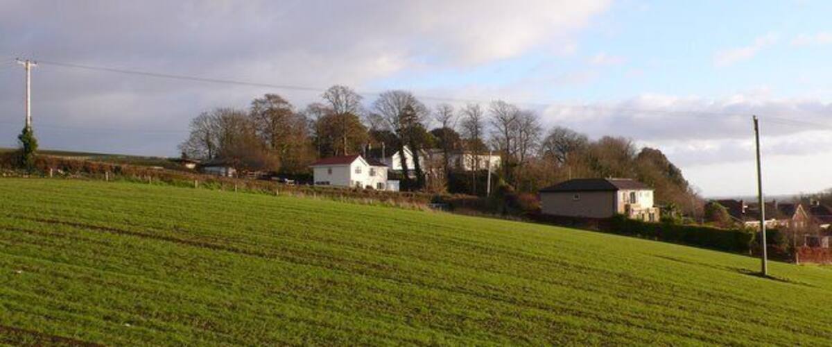 A rural landscape with a green field, white houses, and a cloudy sky.
