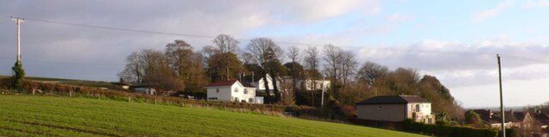 A rural landscape with a green field, white houses, and a cloudy sky.