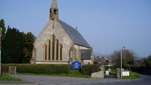 A church with a pointed steeple and a blue sign in front.