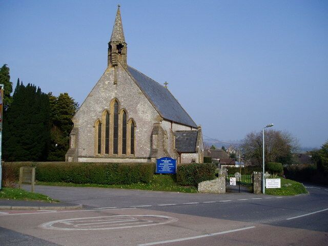 A church with a pointed steeple and a blue sign in front.