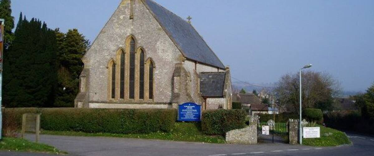 A church with a pointed steeple and a blue sign in front.