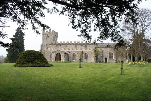 A historic stone building with a tower, surrounded by a well-maintained lawn and trees.