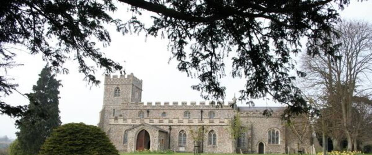 A historic stone building with a tower, surrounded by a well-maintained lawn and trees.