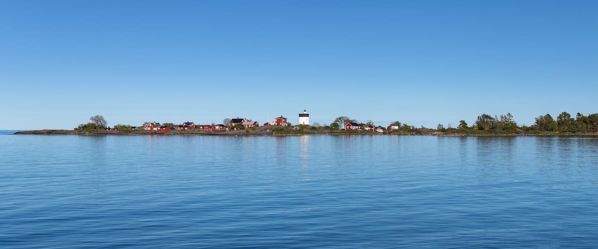 A calm lake with a small island featuring red and white houses and a lighthouse.