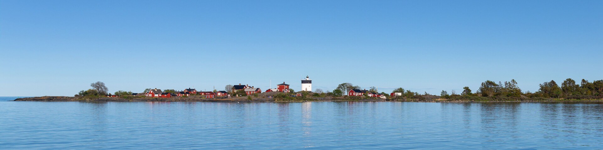 A calm lake with a small island featuring red and white houses and a lighthouse.