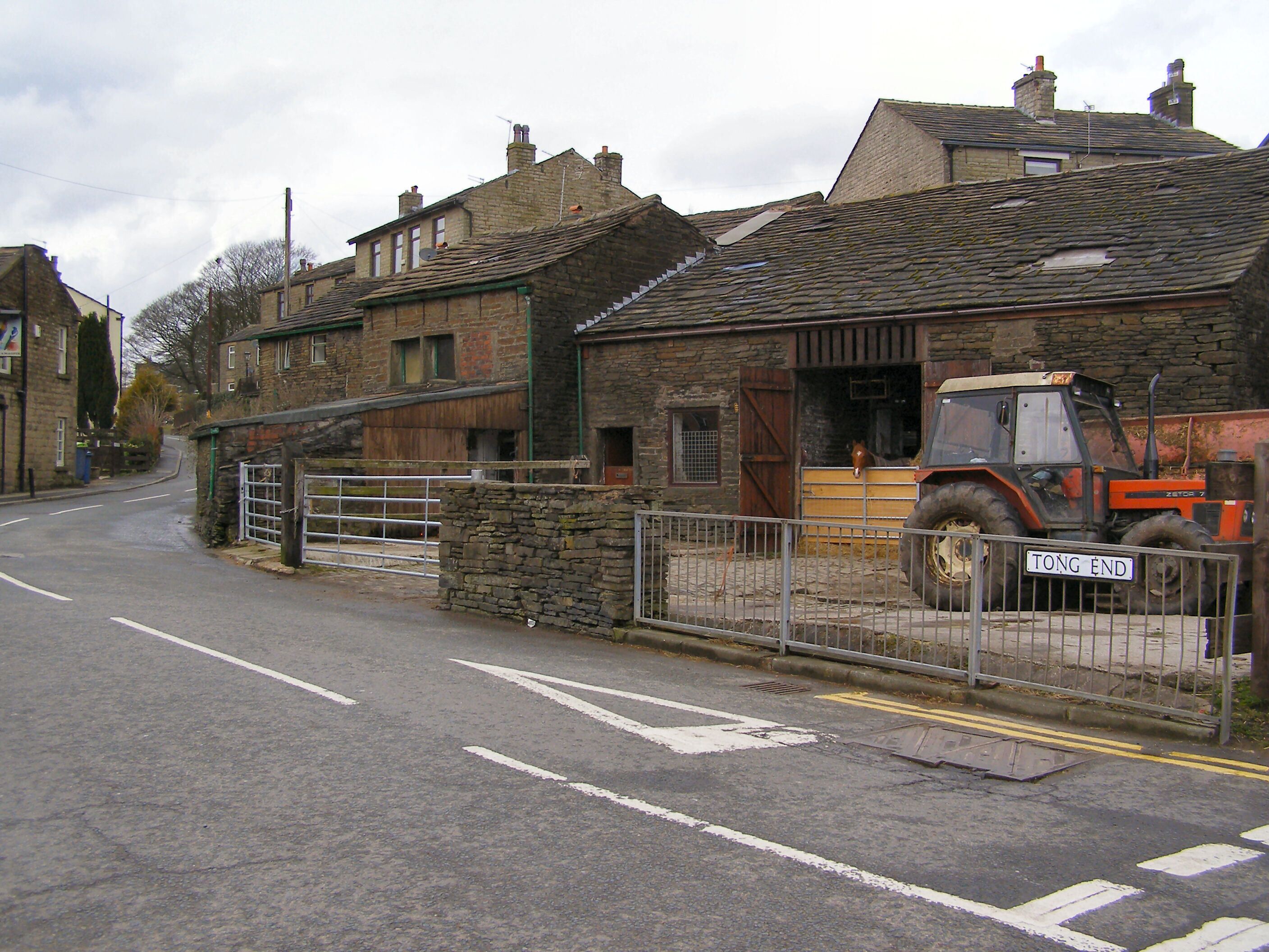 A rural street with stone buildings, a metal gate, and a parked tractor.