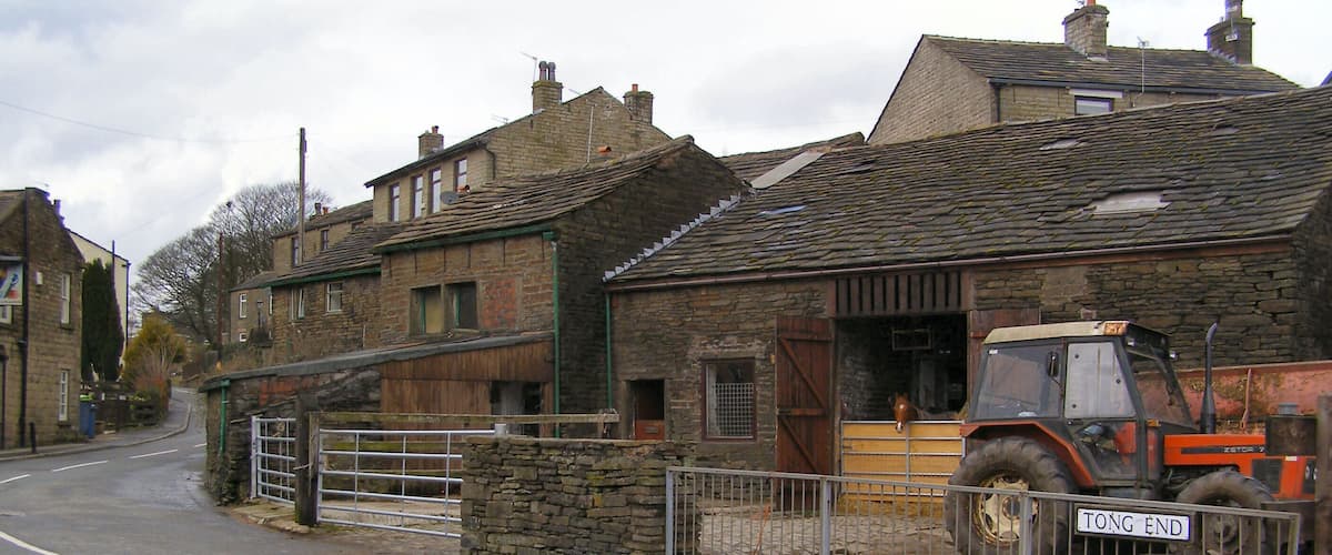 A rural street with stone buildings, a metal gate, and a parked tractor.