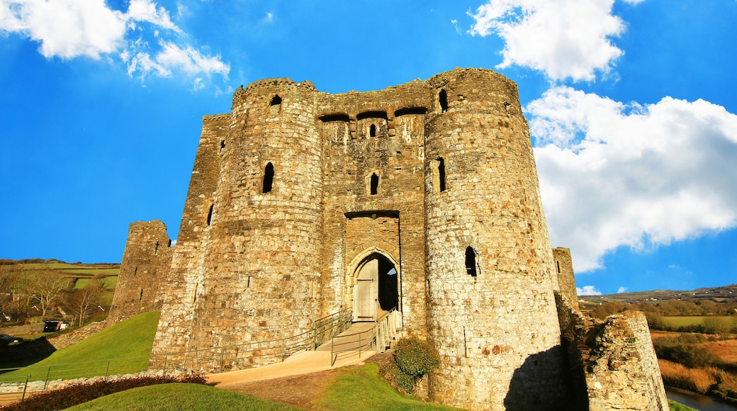 A historic stone castle with multiple towers and a central entrance, surrounded by a grassy landscape under a clear sky.