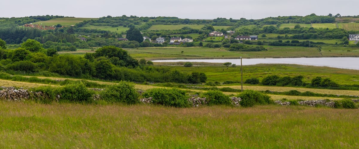 A rural landscape with a lake, rolling hills, scattered houses, and a prominent tower.