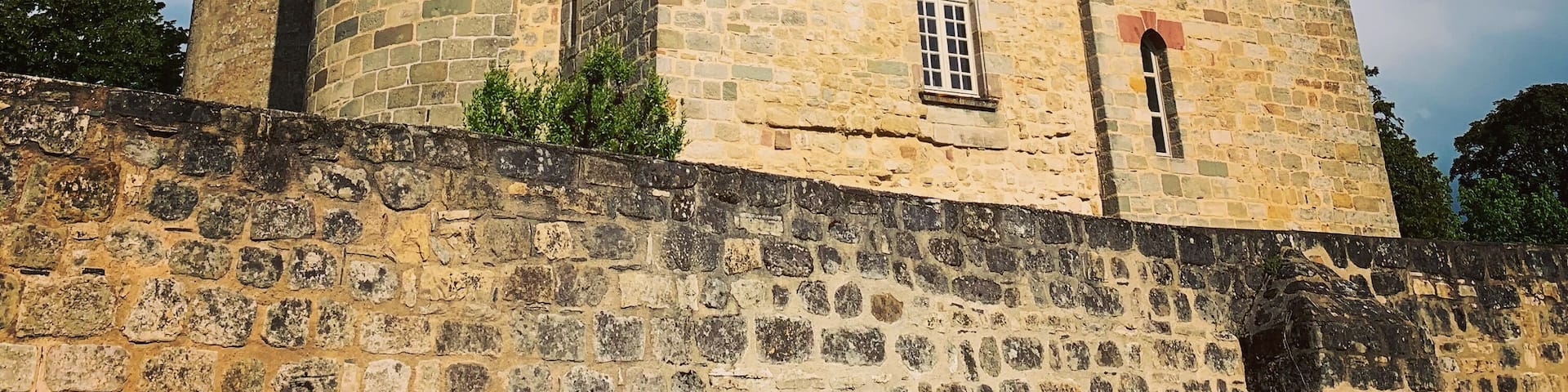 A medieval stone castle with a round tower, arched windows, and a crenellated parapet.