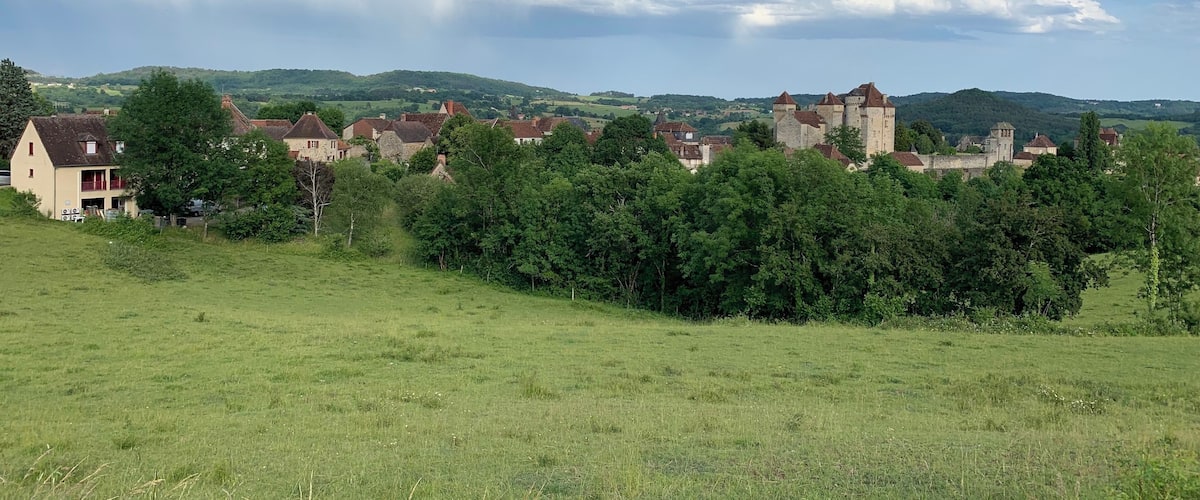 A rural landscape with a castle, houses, and rolling hills.