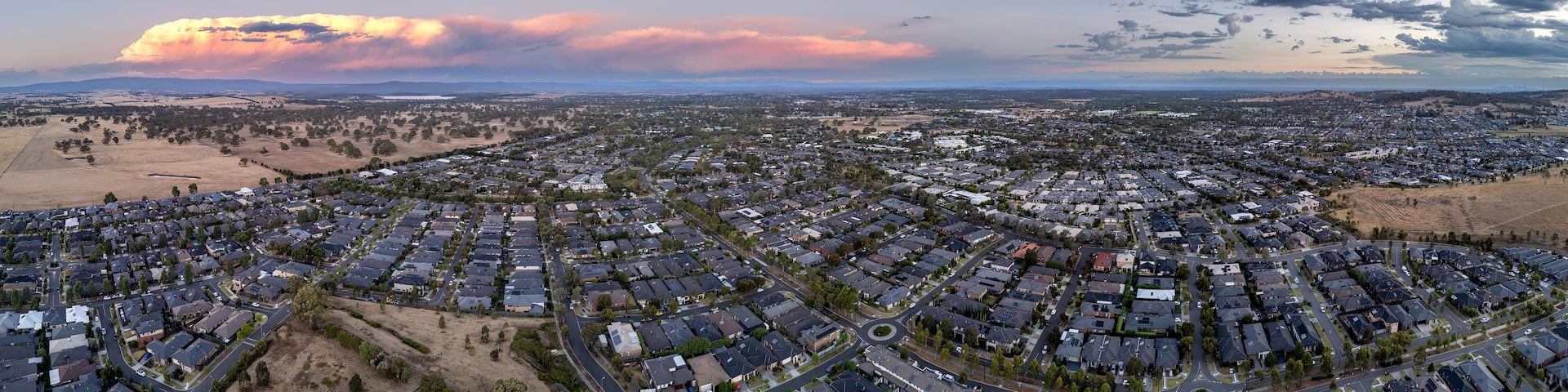 A residential area with houses, roads, and a distant mountain range under a sunset sky.