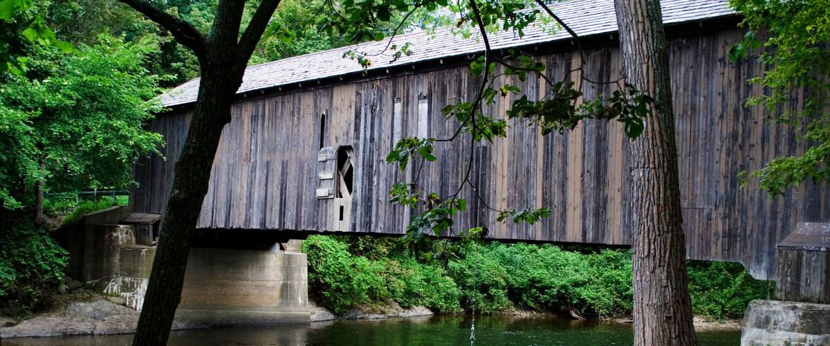 A wooden covered bridge over a calm river, surrounded by lush greenery.