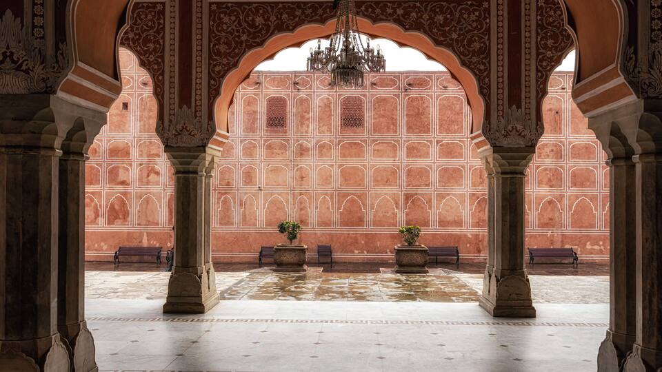 An ornate courtyard with arches, a chandelier, and potted plants.