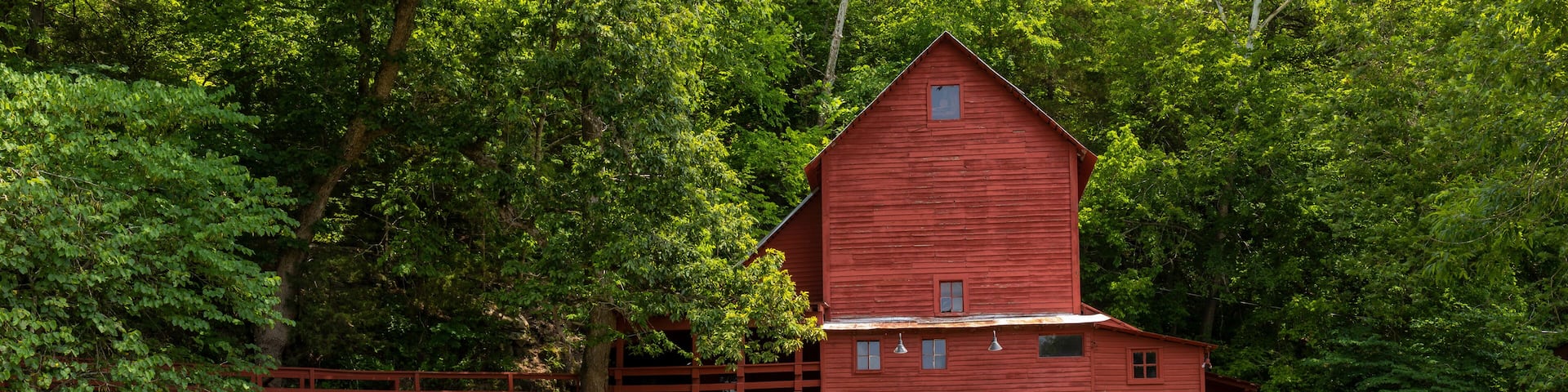 A red watermill with a wooden wheel, surrounded by lush greenery and a small waterfall.
