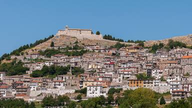 A historic hilltop fortress overlooking a densely packed town with terracotta-roofed buildings.