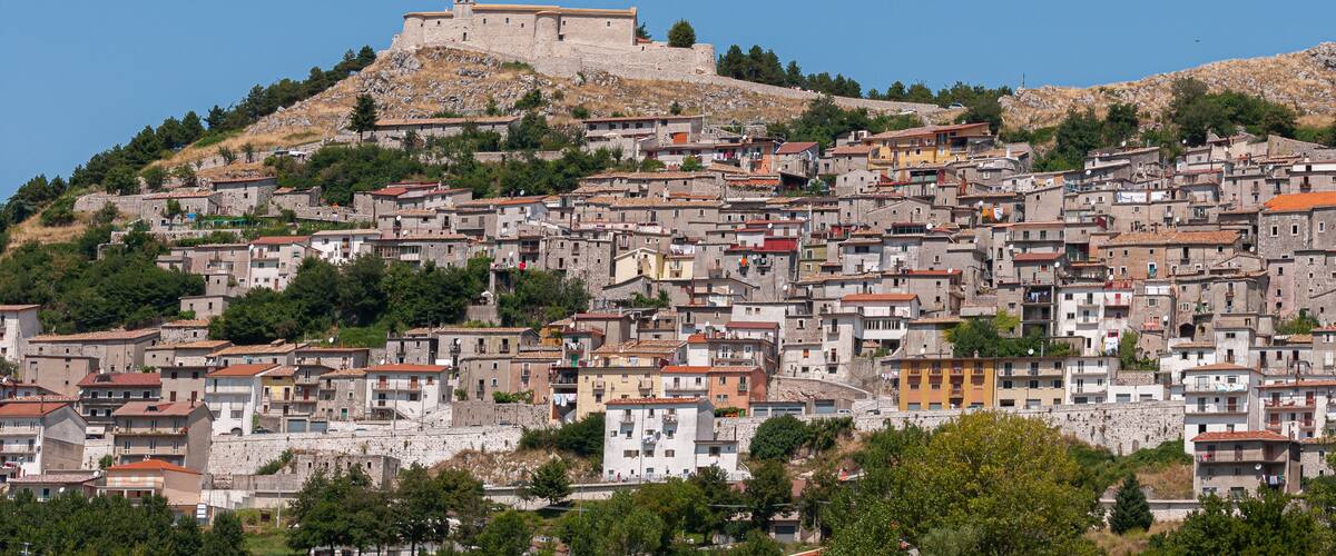 A historic hilltop fortress overlooking a densely packed town with terracotta-roofed buildings.