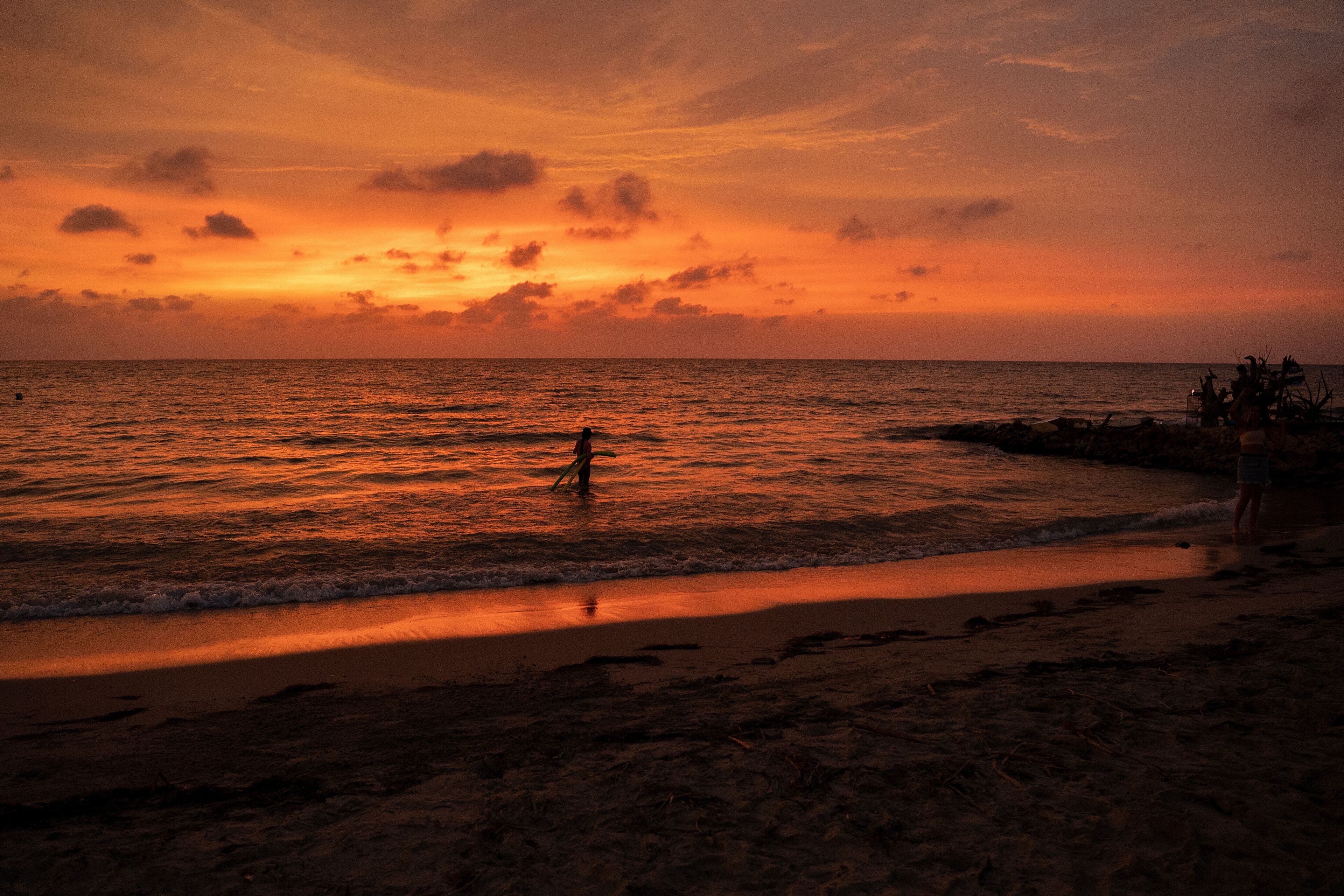 A beach at sunset with a person standing in the water.