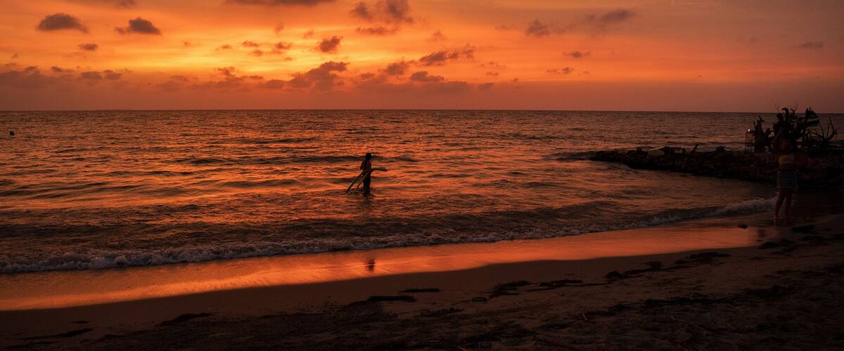 A beach at sunset with a person standing in the water.