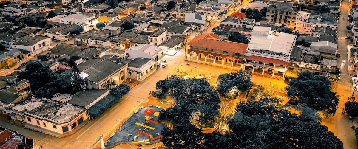 An aerial view of a cityscape with a prominent building with a red roof, surrounded by trees and a sports court.
