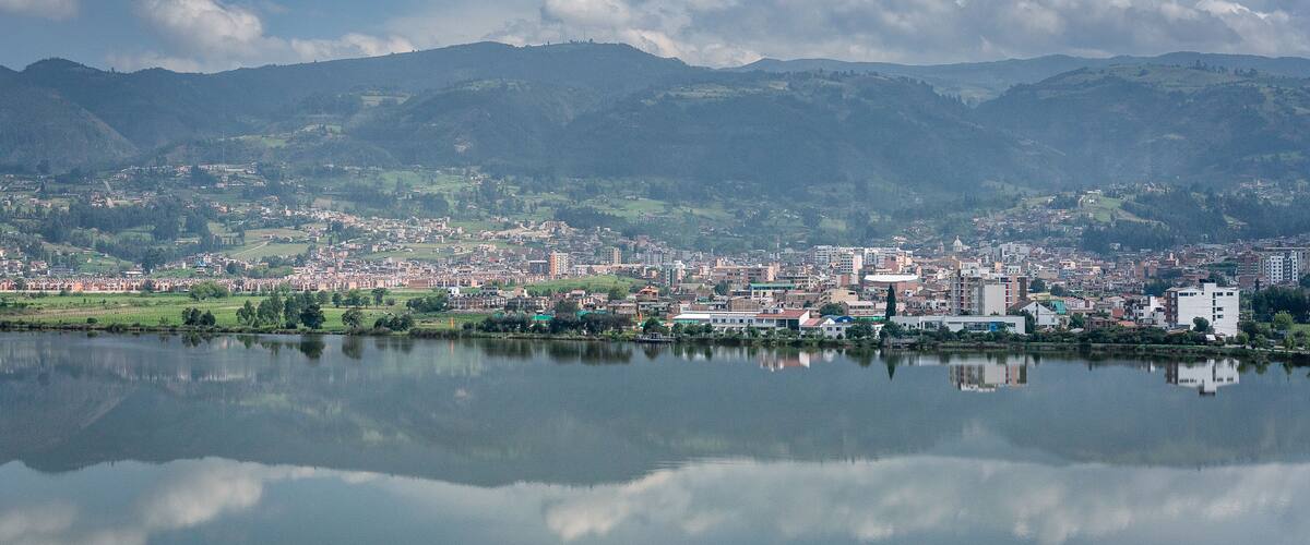 A cityscape with a lake reflecting buildings and mountains in the background.