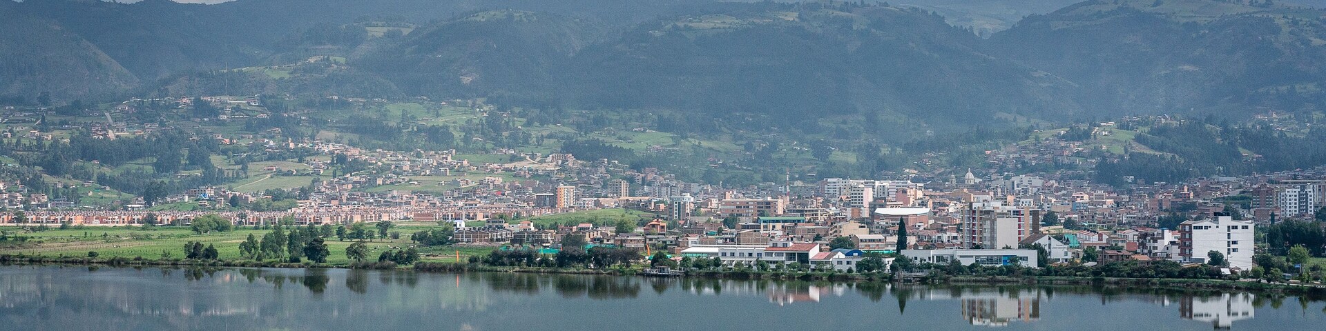 A cityscape with a lake reflecting buildings and mountains in the background.