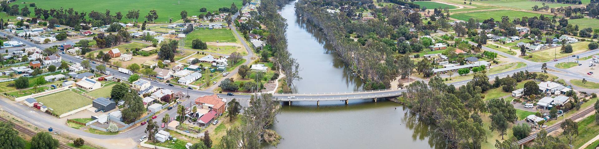 Aerial view of two bridges crossing a tree lined river dividing a country town
