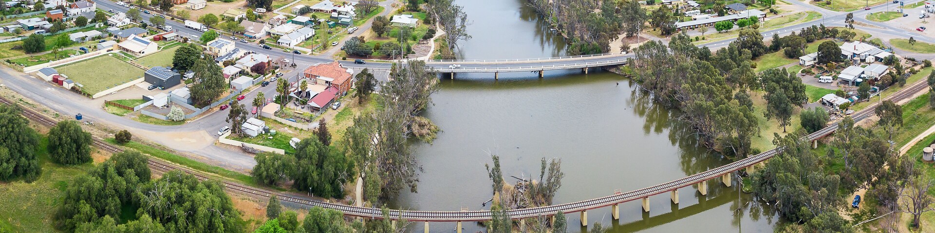 Aerial view of two bridges crossing a tree lined river dividing a country town