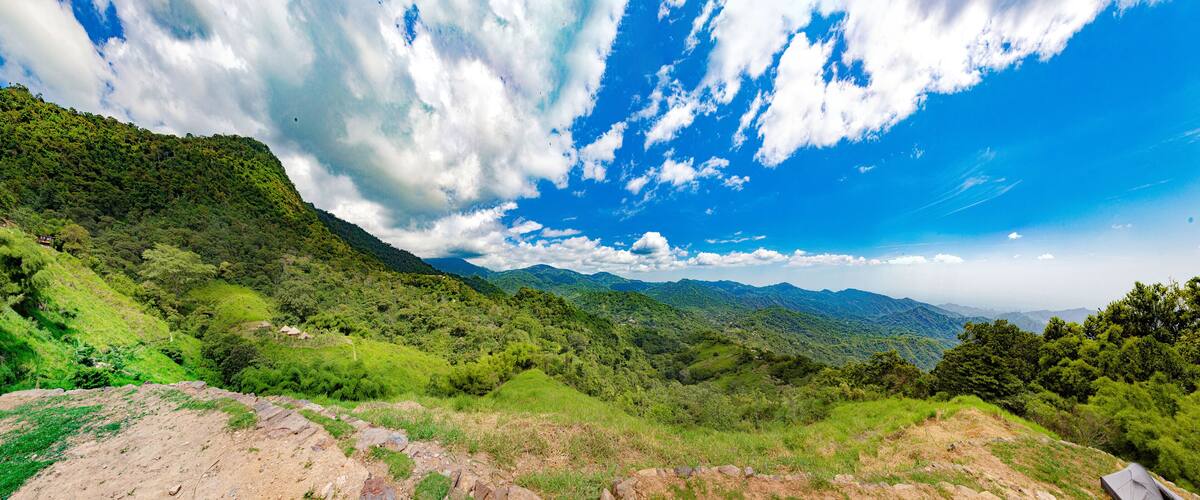 A mountainous landscape with lush greenery and a clear blue sky with scattered clouds.
