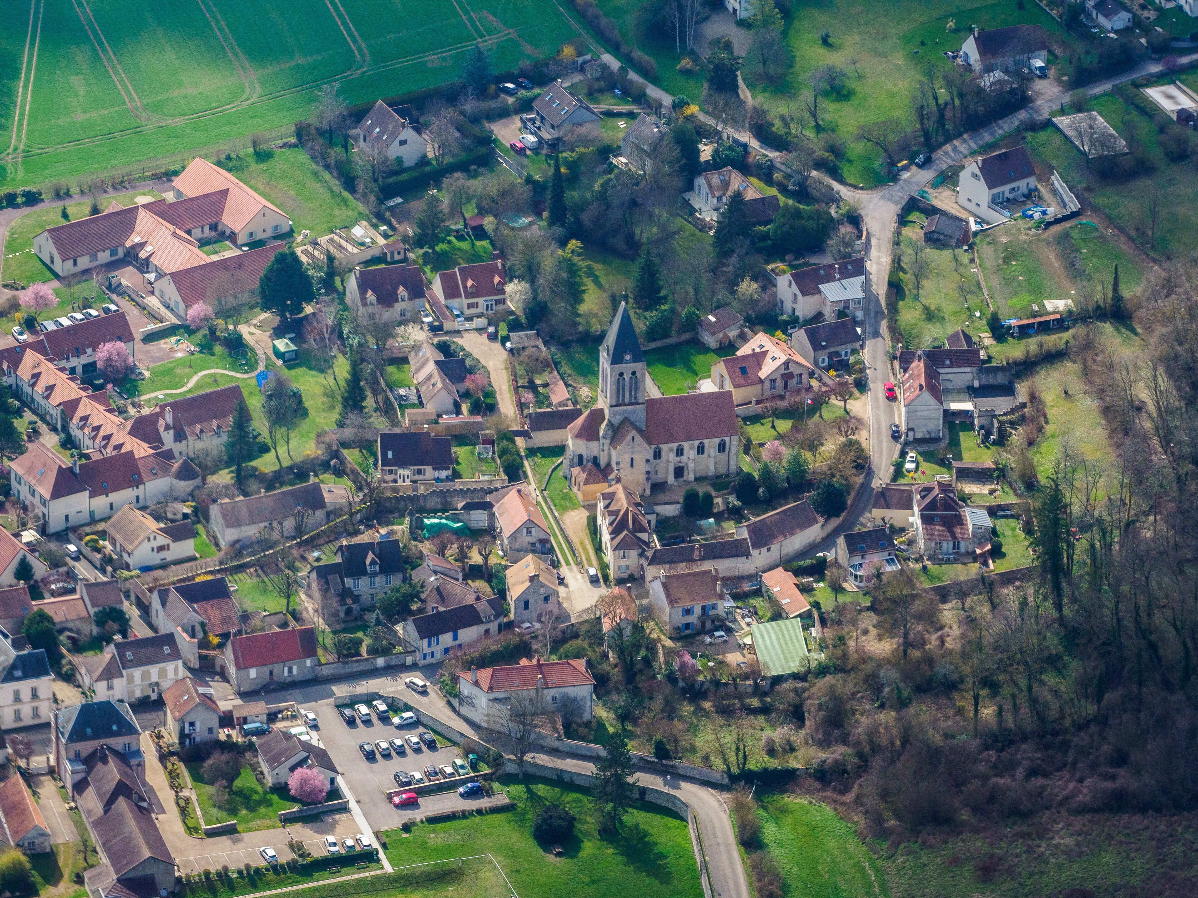 An aerial view of a historic village with a church, residential houses, and a parking area.