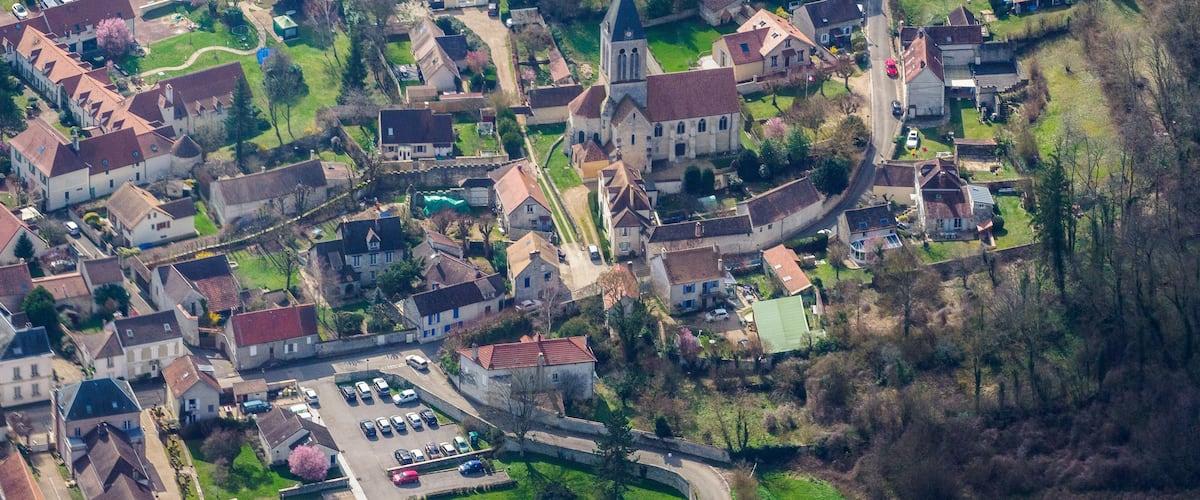 An aerial view of a historic village with a church, residential houses, and a parking area.