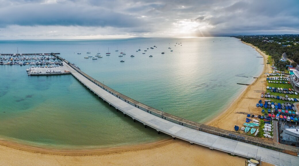Aerial panorama of long pier leading to moored boats at marina. Beautiful turquoise water and beach